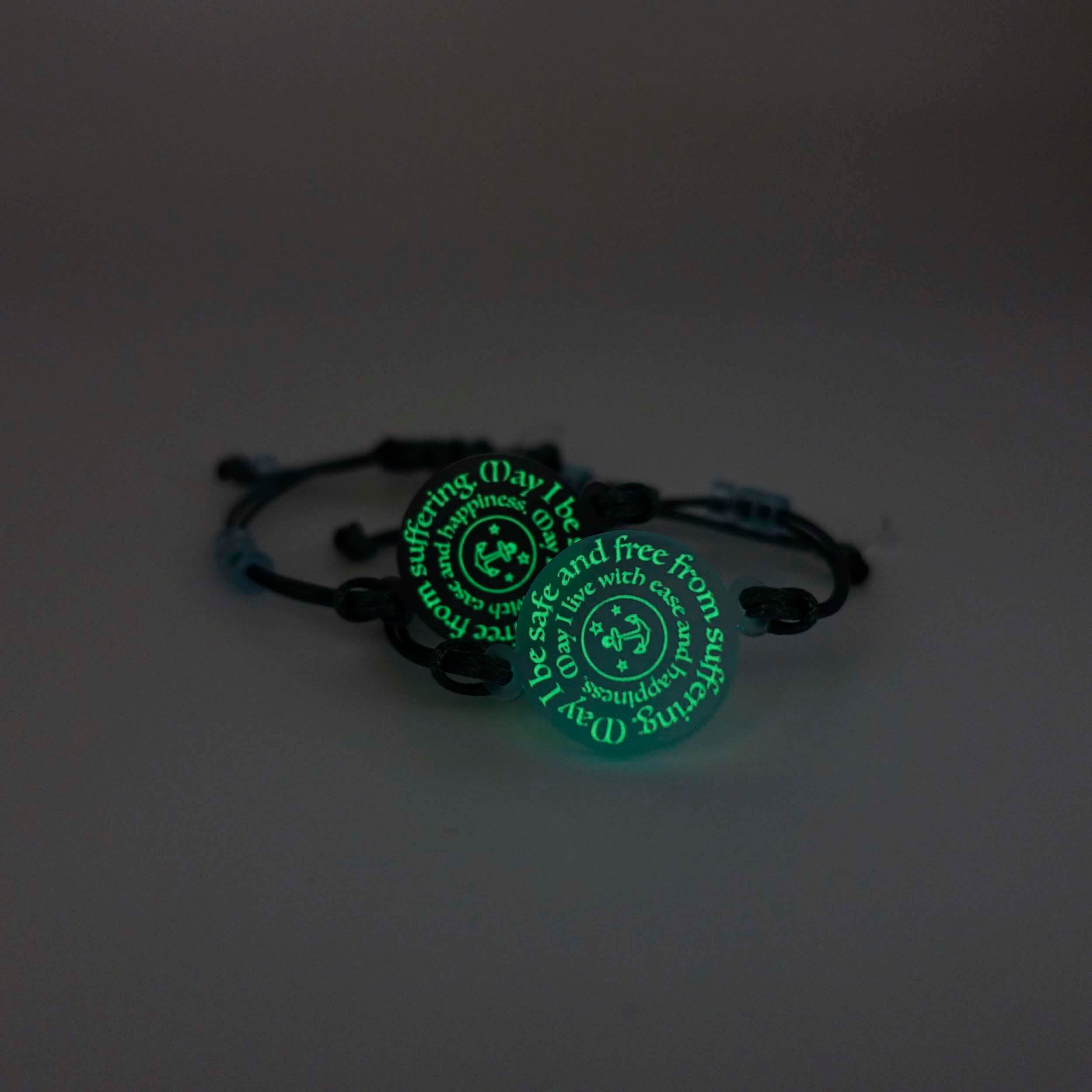 May I Be Safe bracelets in sea foam and shale shown glowing in the dark.