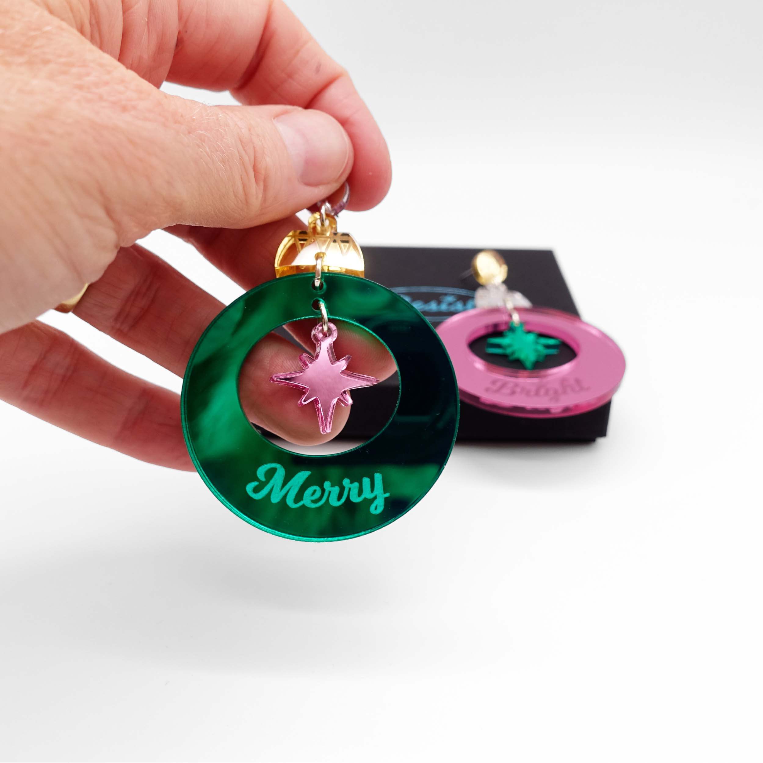 Merry & Bright Christmas bauble earrings in electric green and pink mirror, shown held in my hand for scale.