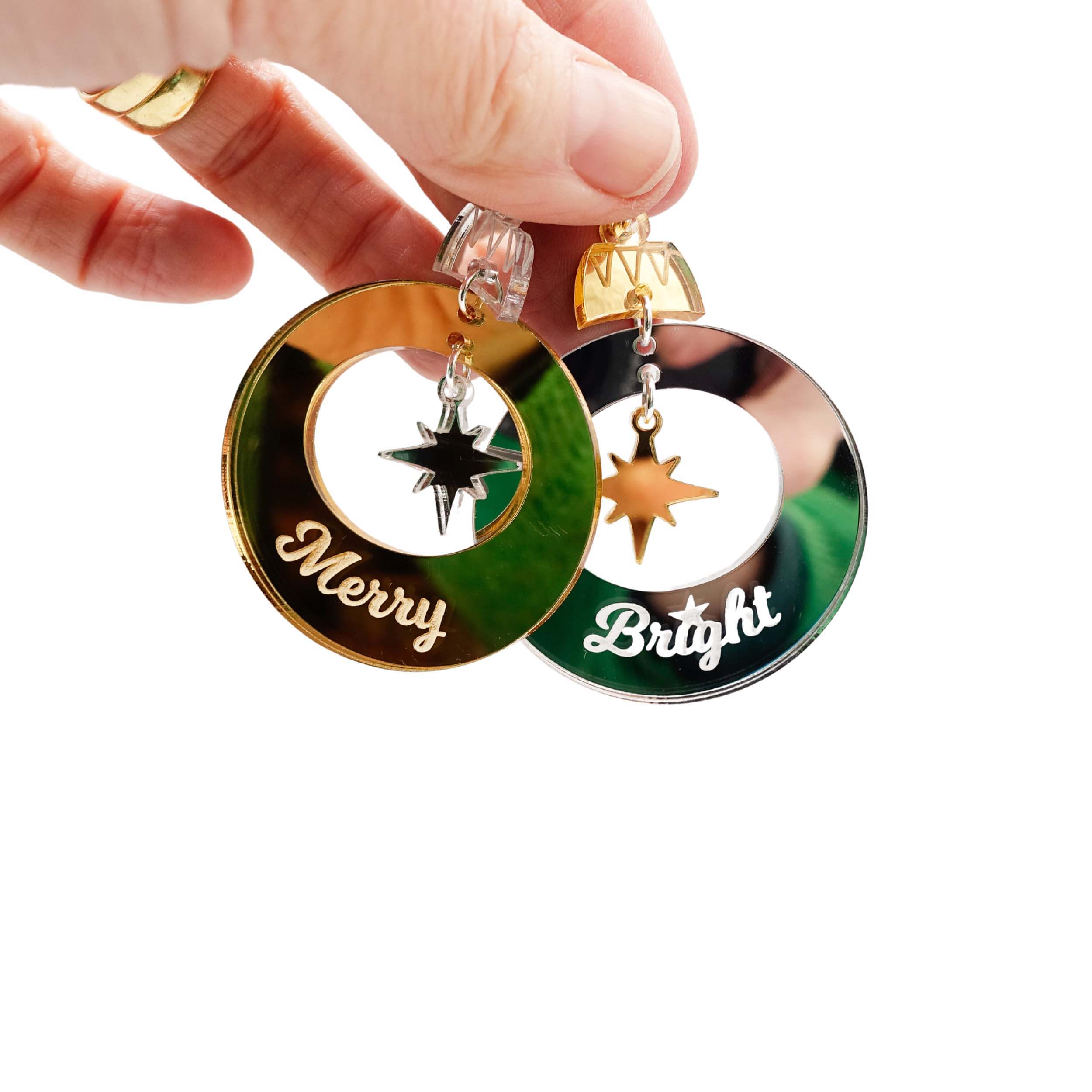 Merry & Bright Christmas bauble earrings in silver and gold shown held in my hand against a white background.