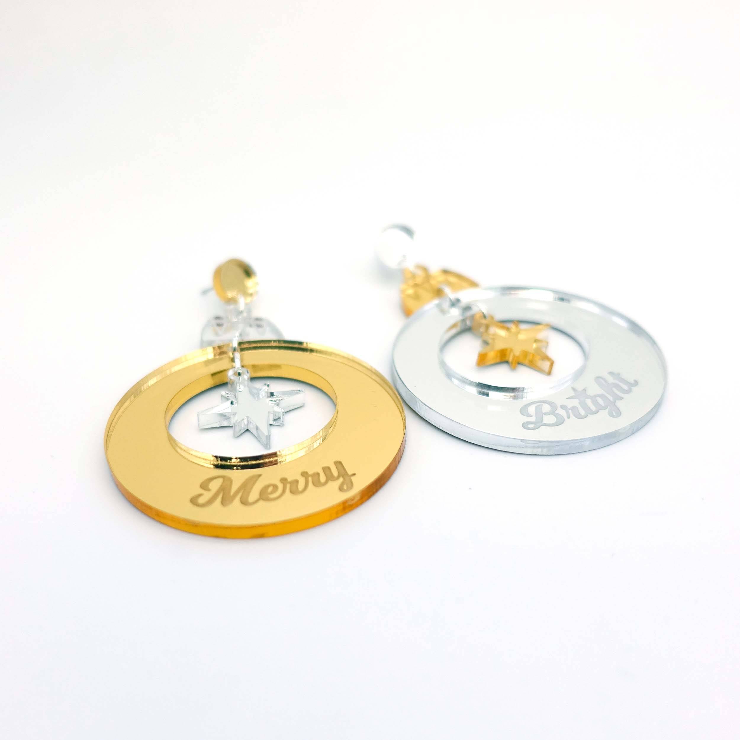 Merry & Bright Christmas bauble earrings in gold and silver shown laying on a white surface.