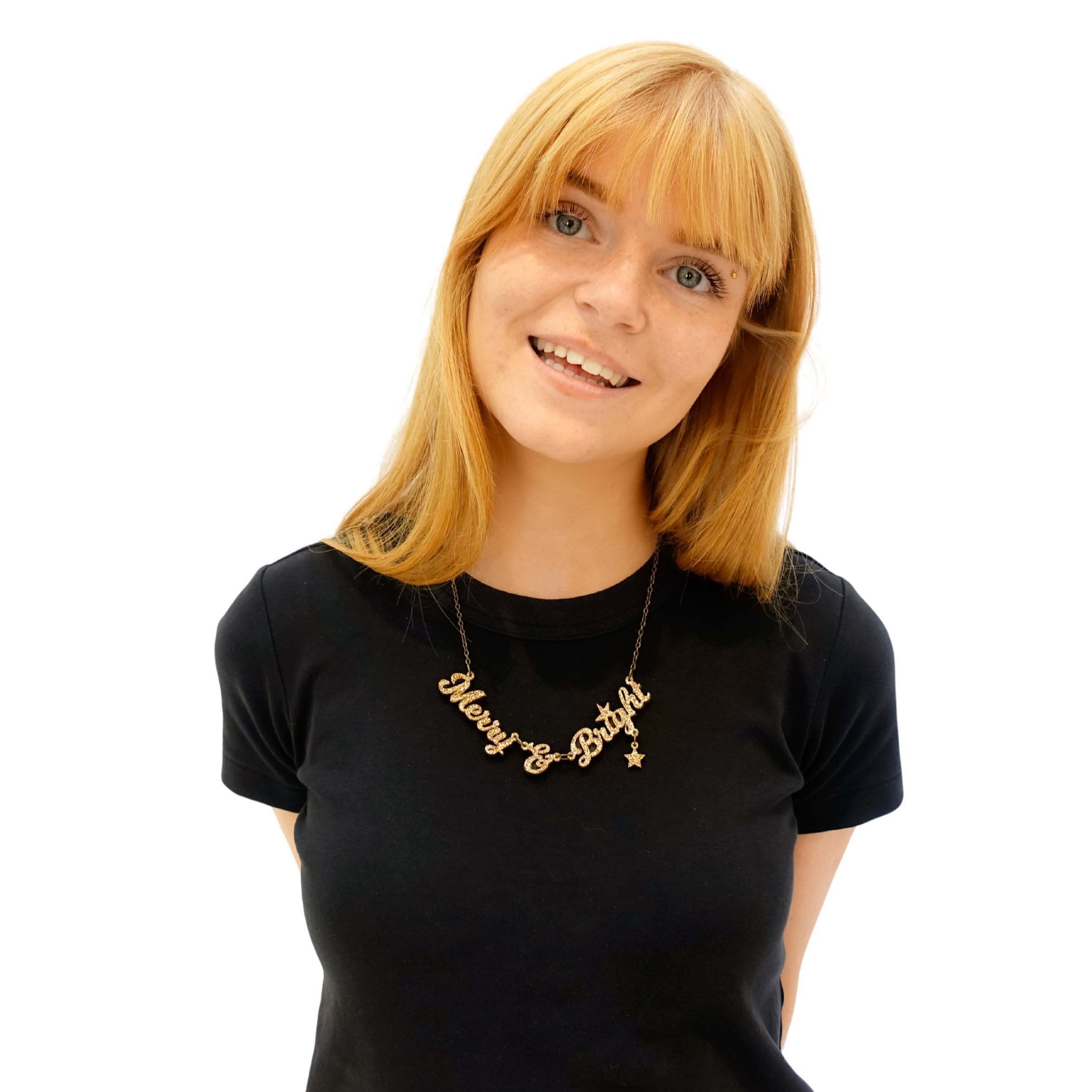 Eliza smiles wearing a Merry & Bright necklace in gold glitter.