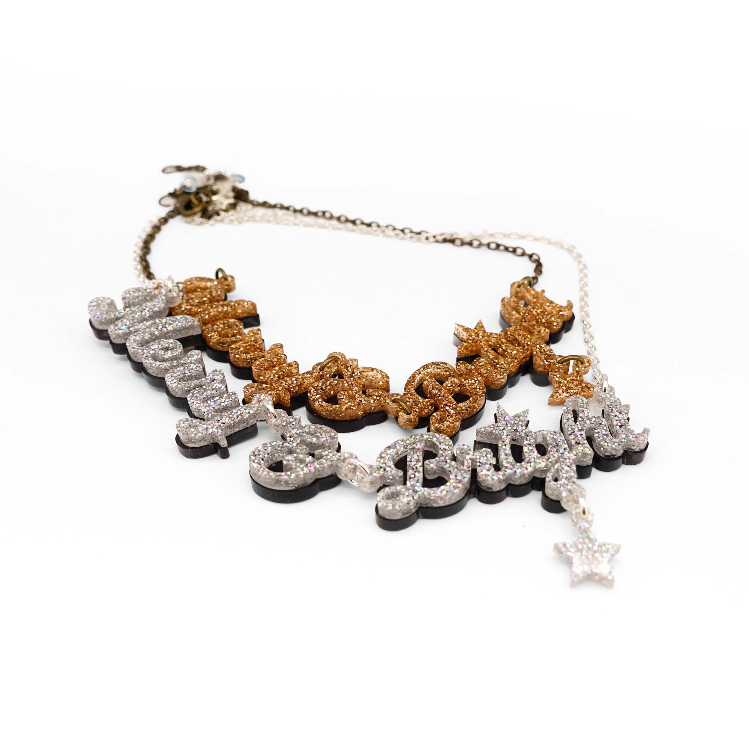 Silver and gold glitter Merry & Bright necklaces shown laying on a white surface.