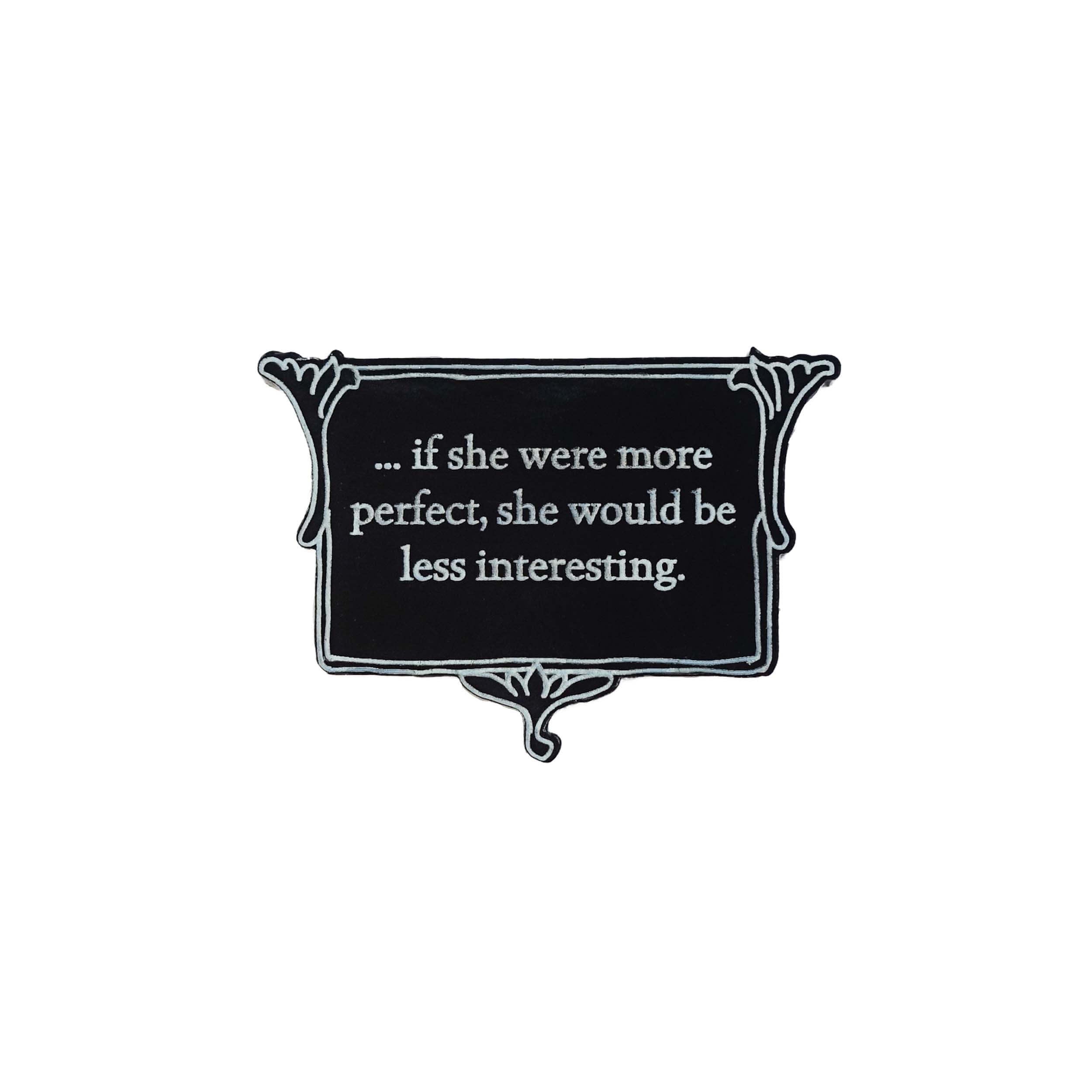 A matte black brooch etched with glow-in-the-dark pigment that says, 'if she were more perfect, she would be less interesting.'  This quote comes from Anne Brontë's The Tenant of Wildfell Hall and is part of The Brontë Collection at Wear and Resist.