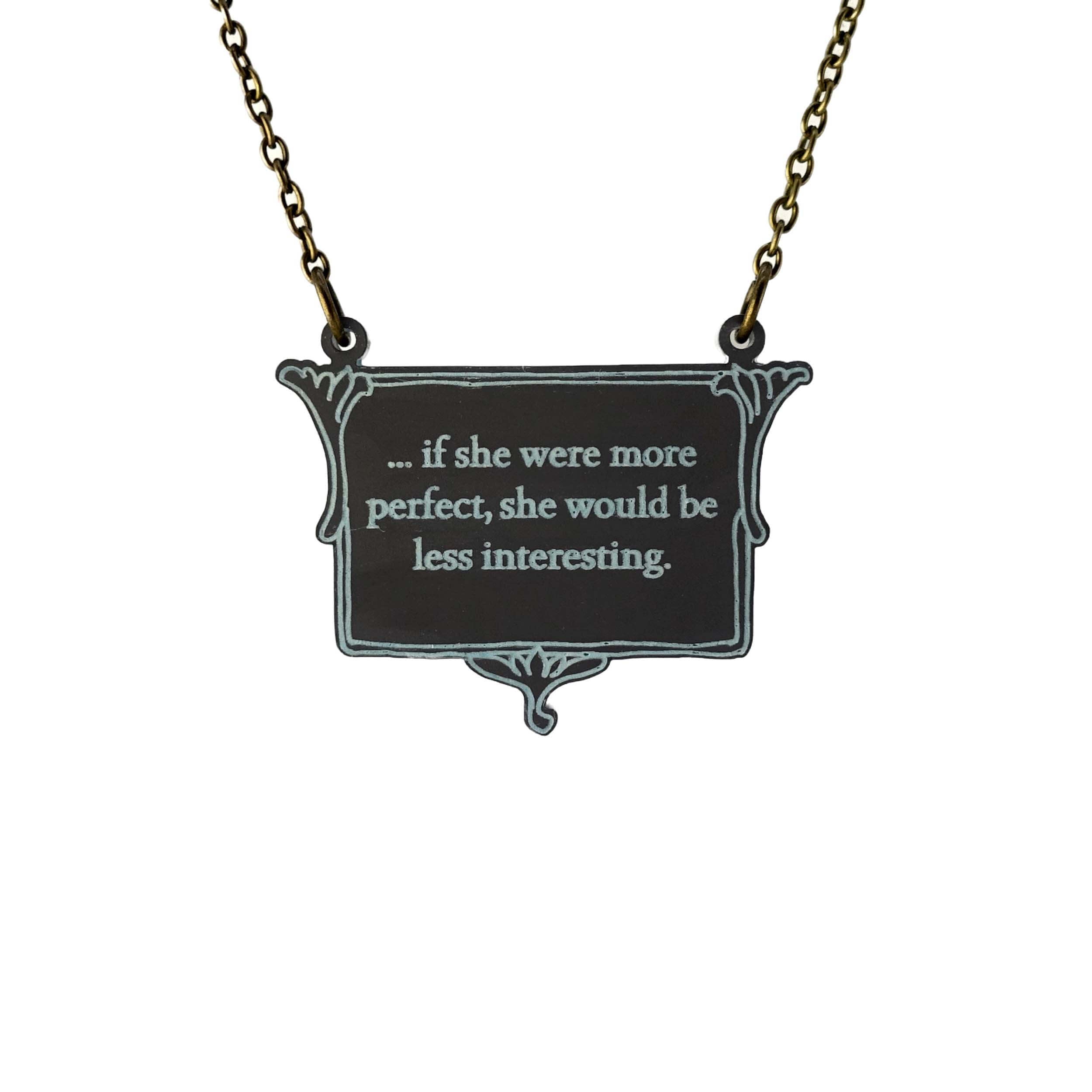 A vintage style slate frost necklace etched with glow-in-the-dark pigment that says, 'if she were more perfect, she would be less interesting' from Anne Brontë's The Tenant of Wildfell Hall, shown on an antique gold chain hanging against a white background.