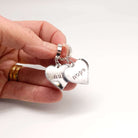 Nah Nope heart shaped huggie hoop earrings in silver mirror shown held in my hand with a white surface behind.