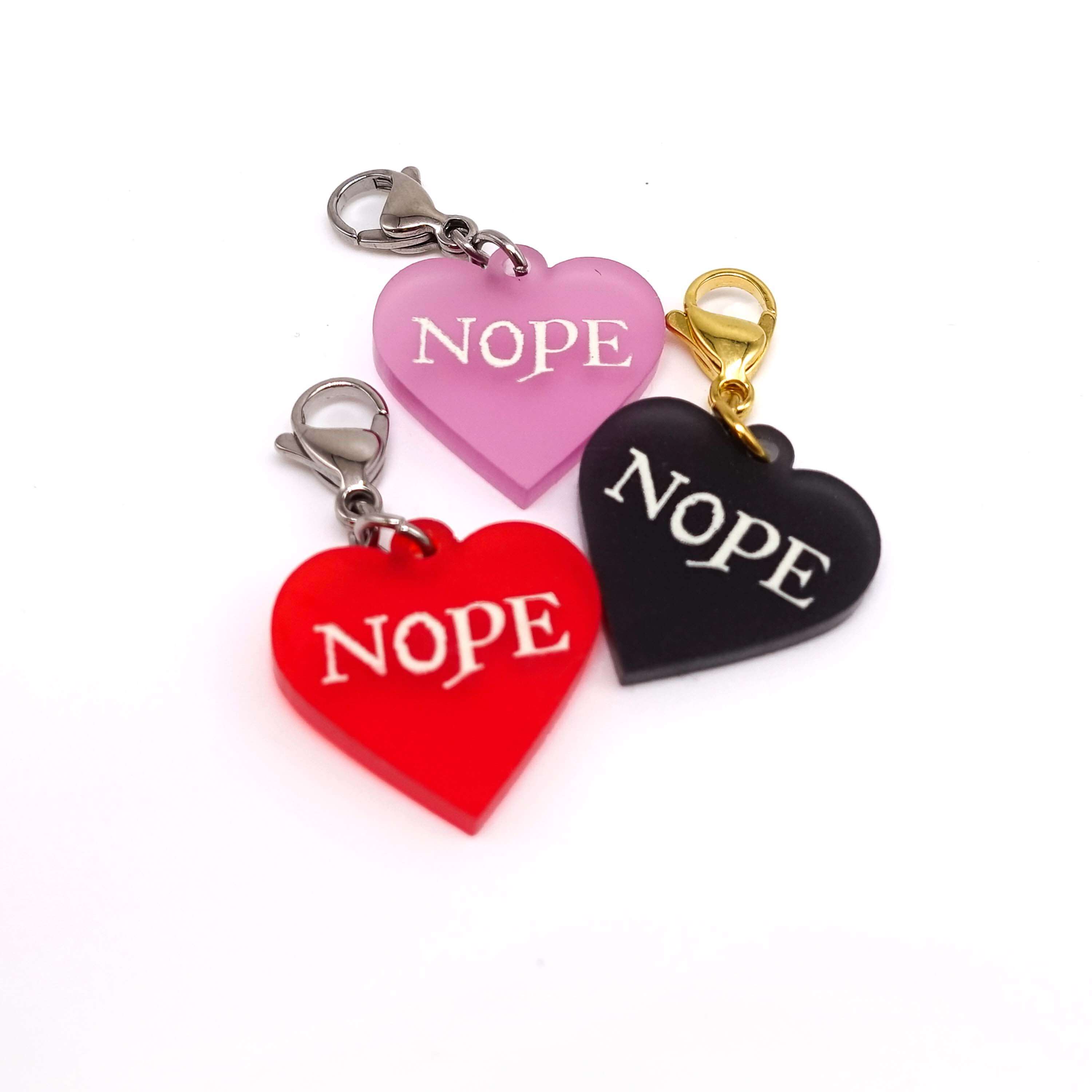 Heart charms in chilli frost, pink frost and slate frost etched in glow-in-the-dark pigment with the word 'Nope'