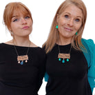 Eliza wears the CA VA PAS necklace and matching rose gold French drop earrings, while Sarah wears the swearier P*TAINE DE M*RDE necklace, and matching electric green French drop earrings from the Paris Collection.