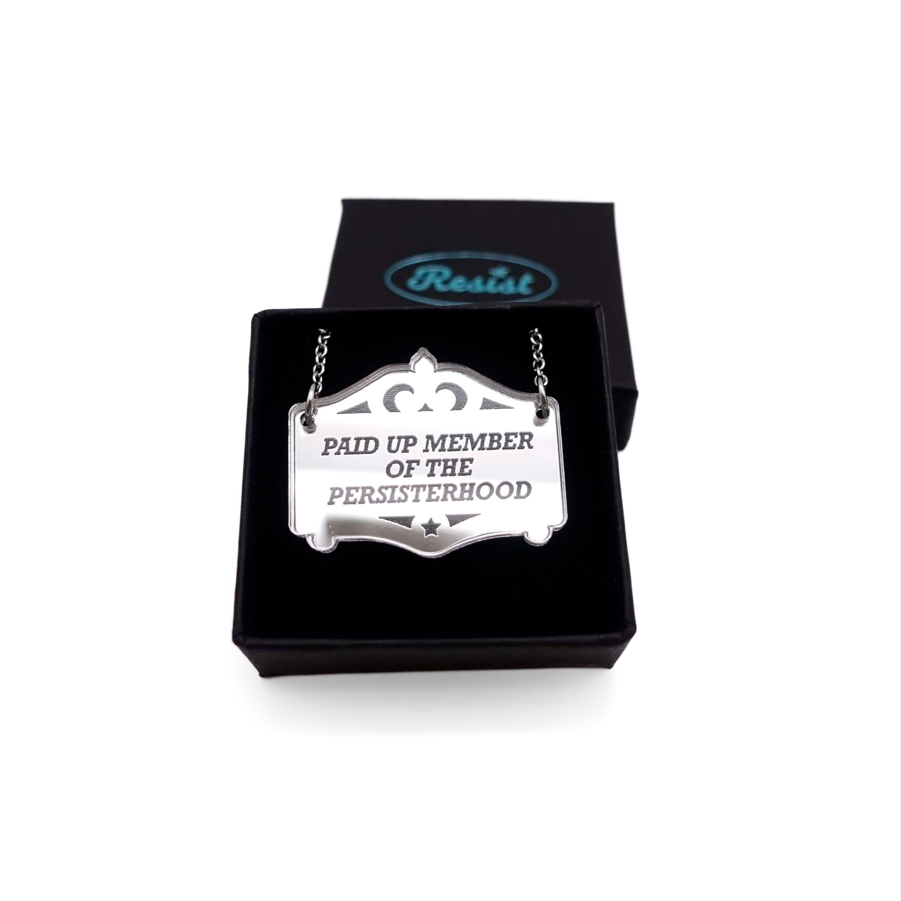 A silver Mirror Cowboy necklace etched with Paid up member of the Persisterhood, shown in a small Wear and Resist gift box.