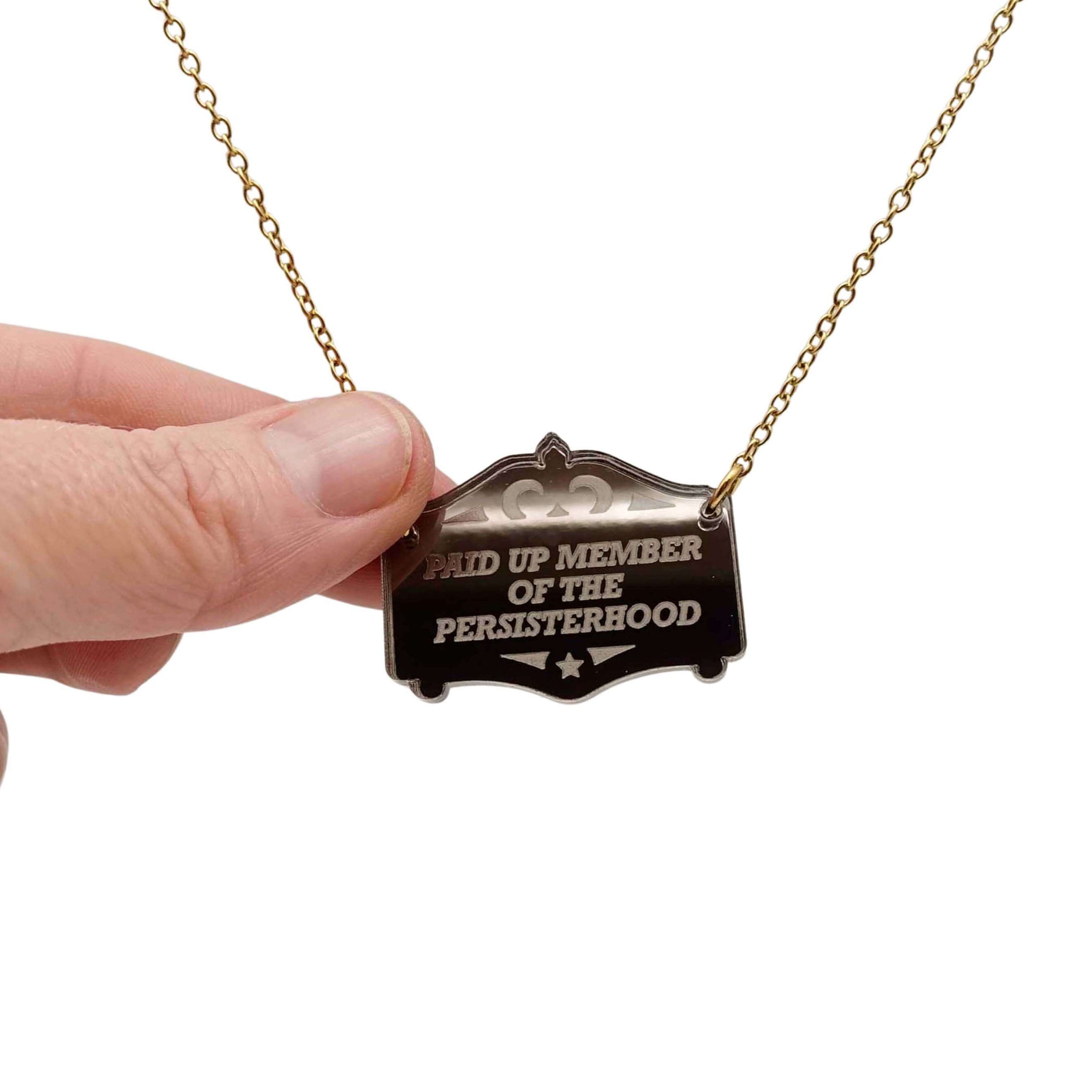 A bronze Paid up member of the Persisterhood necklace, shown hanging on a gold-plated stainless steel chain, with my hand for scale.