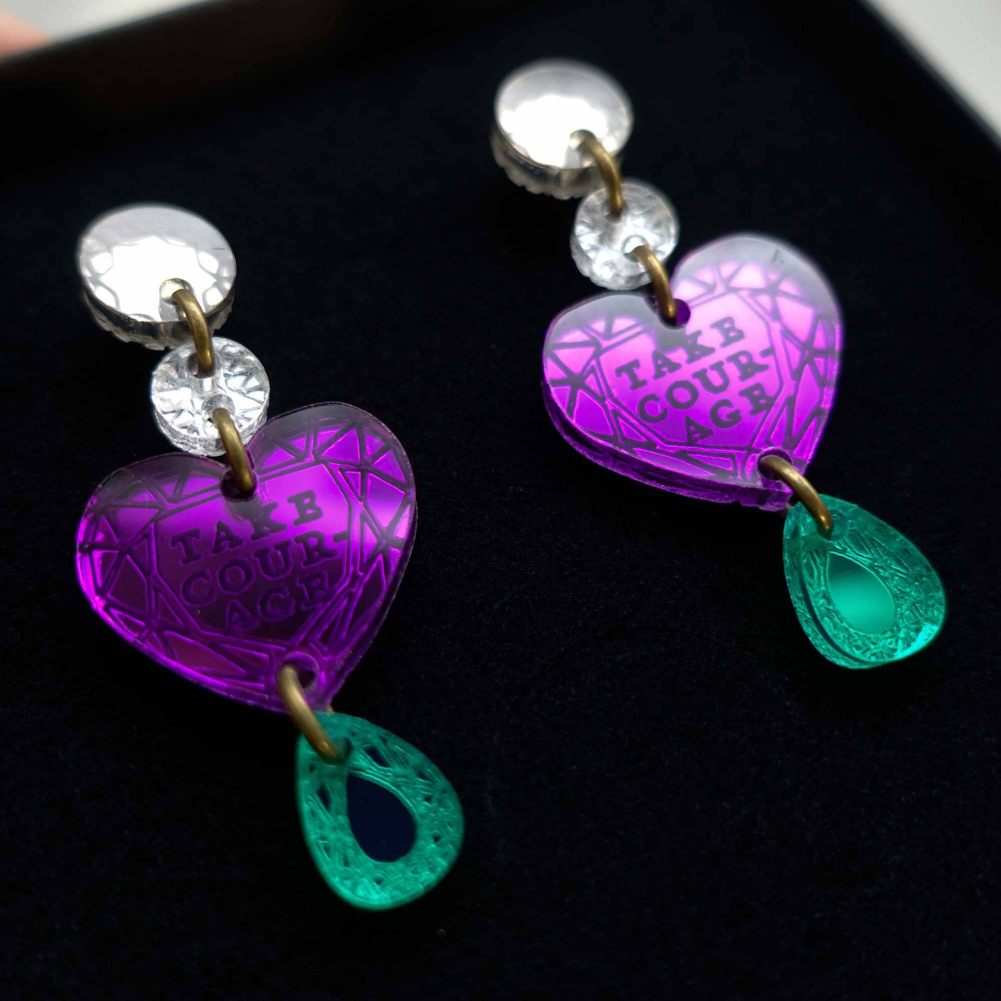 A close up of the Take Courage heart drop earrings in a Wear and Resist gift box.