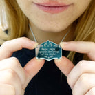 Eliza holds a Rage, rage against the Lying of the Right mirror cowboy necklace in silver.