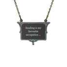A vintage style slate frost necklace etched with glow-in-the-dark pigment that says, 'Reading is my favourite occupation ...' a quote from Anne Brontë's Agnes Grey, shown on an antique gold chain hanging against a white backround.