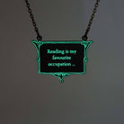 A vintage style slate frost necklace etched with glow-in-the-dark pigment that says, 'Reading is my favourite occupation ...' a quote from Anne Brontë's Agnes Grey, shown on an antique gold chain glowing in the dark.