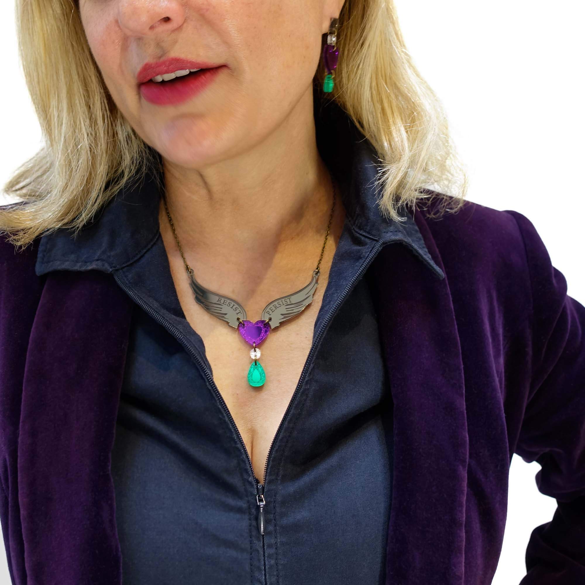 Andrea wears the Resist Persist winged heart necklace with matching Take Courage heart drop earrings.