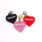 Heart charms in chilli frost, pink frost and slate frost etched in glow-in-the-dark pigment with the word 'Resist'