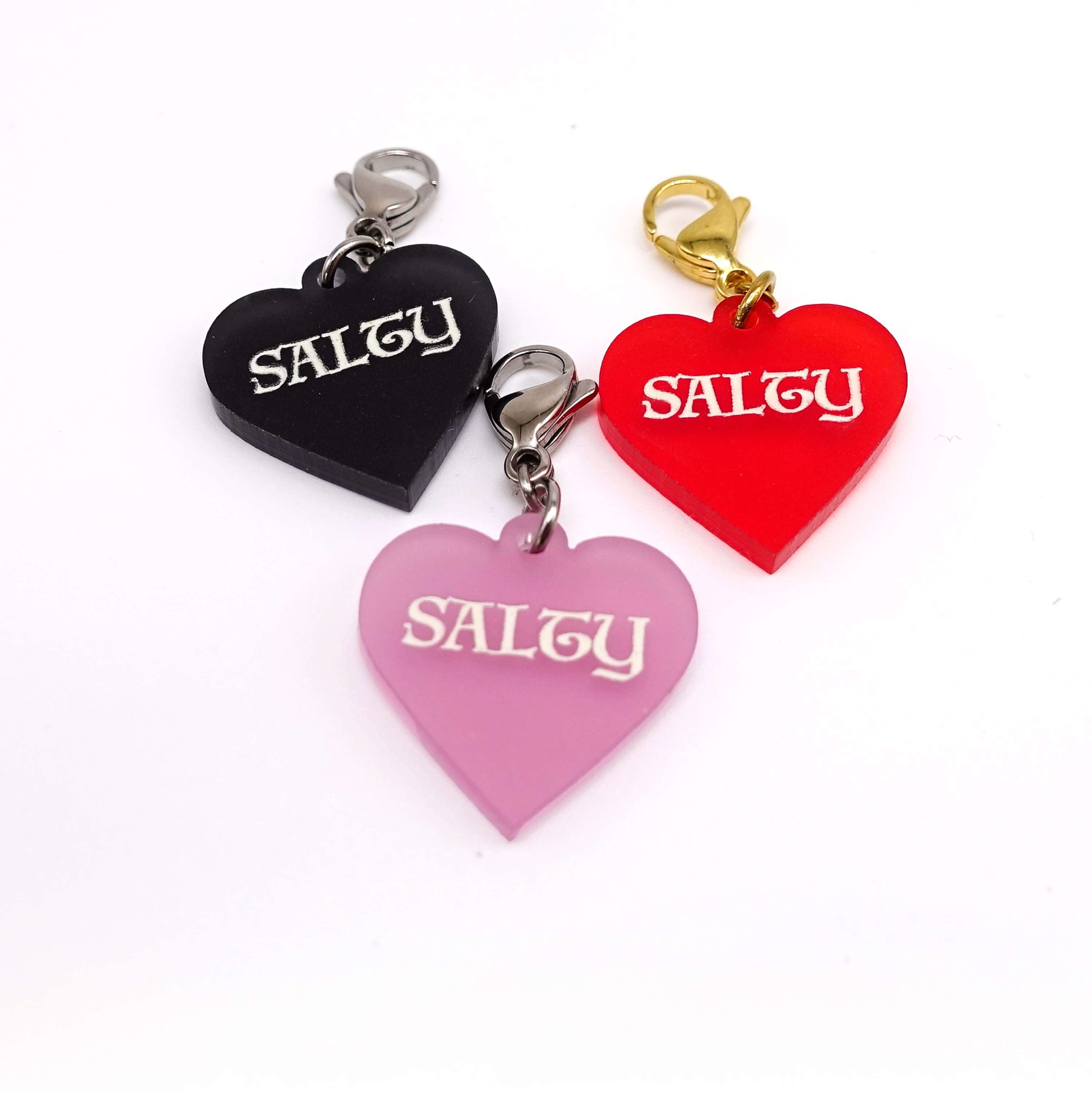 Heart charms in chilli frost, pink frost and slate frost etched in glow-in-the-dark pigment with the word 'Salty