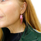 Sarah wears large Lightning Bolt hoop earrings in pink mirror shown against a white background.