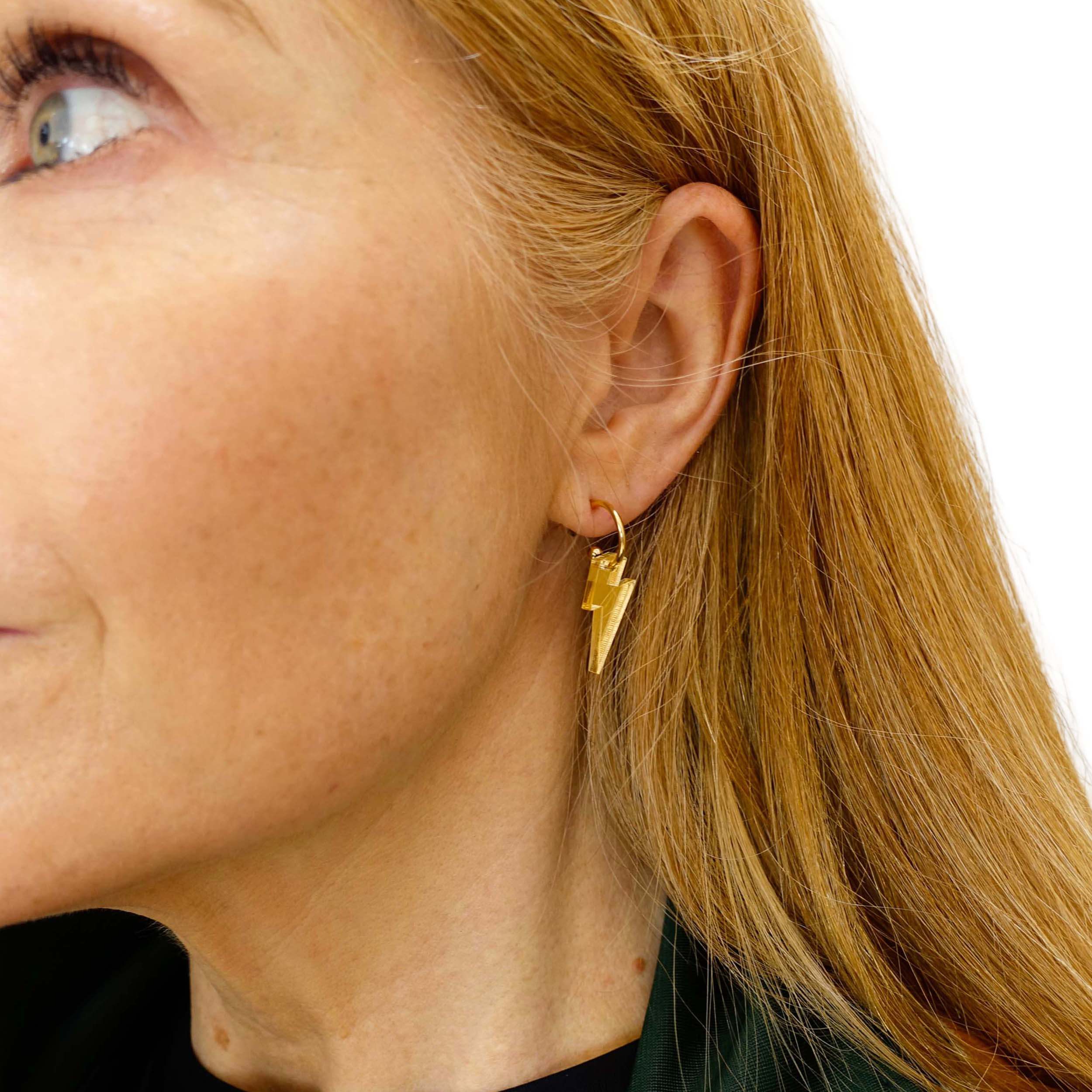 Sarah wears small gold mirror lightning bolt hoops on gold plated hoops.