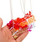 A group of Splendid necklaces in all the different colours shown with my hand behind for scale hanging against a white background.