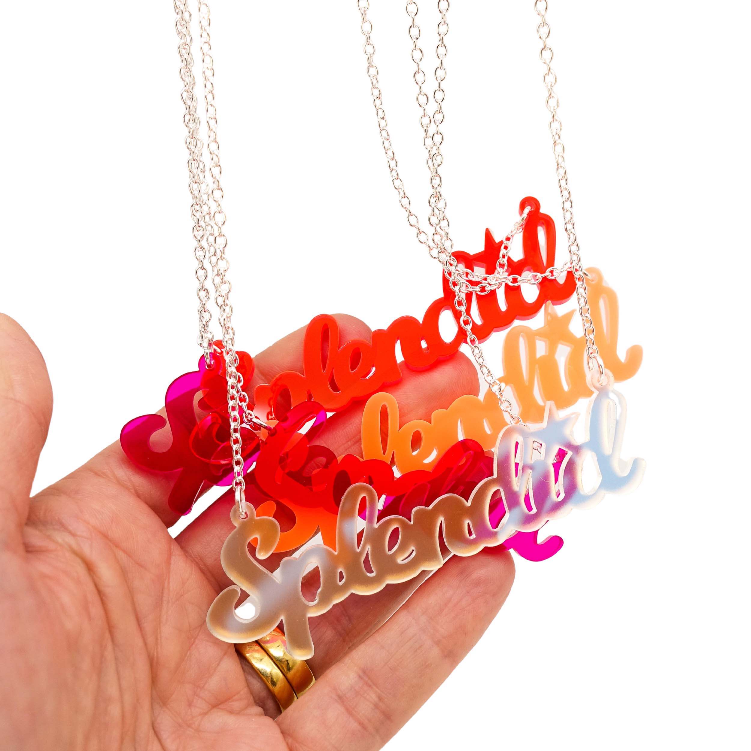 A group of Splendid necklaces in all the different colours shown with my hand behind for scale hanging against a white background.