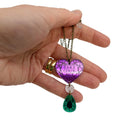 My hand holding the Take Courage heart drop necklace against a white background.