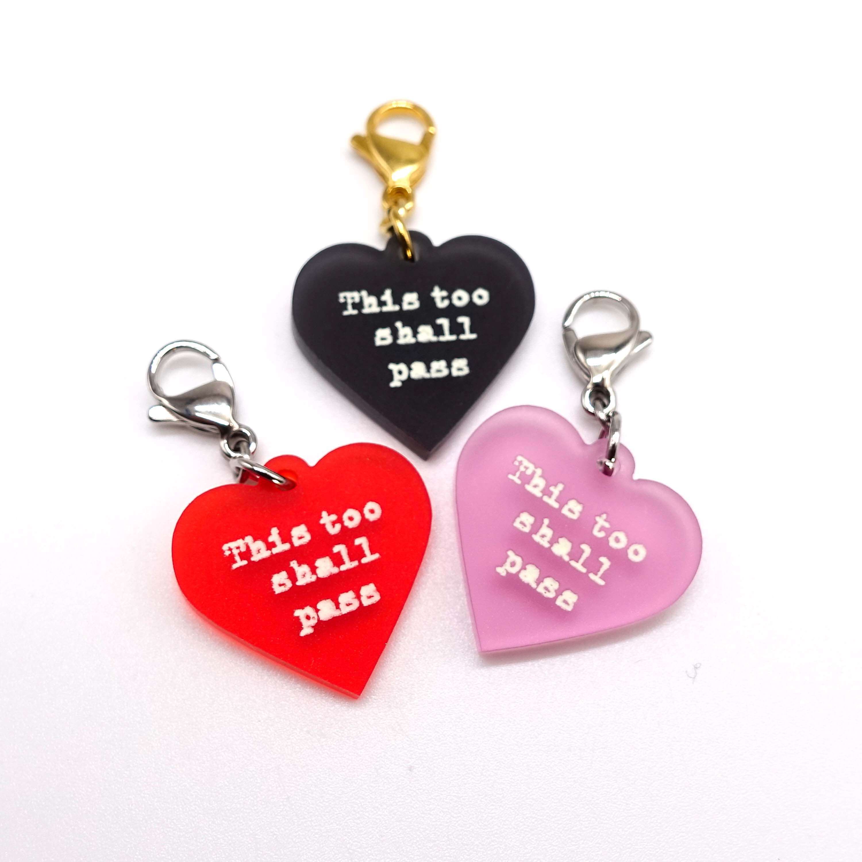 Heart charms etched and hand-painted with the words This too shall pass in glow in the dark pigment.