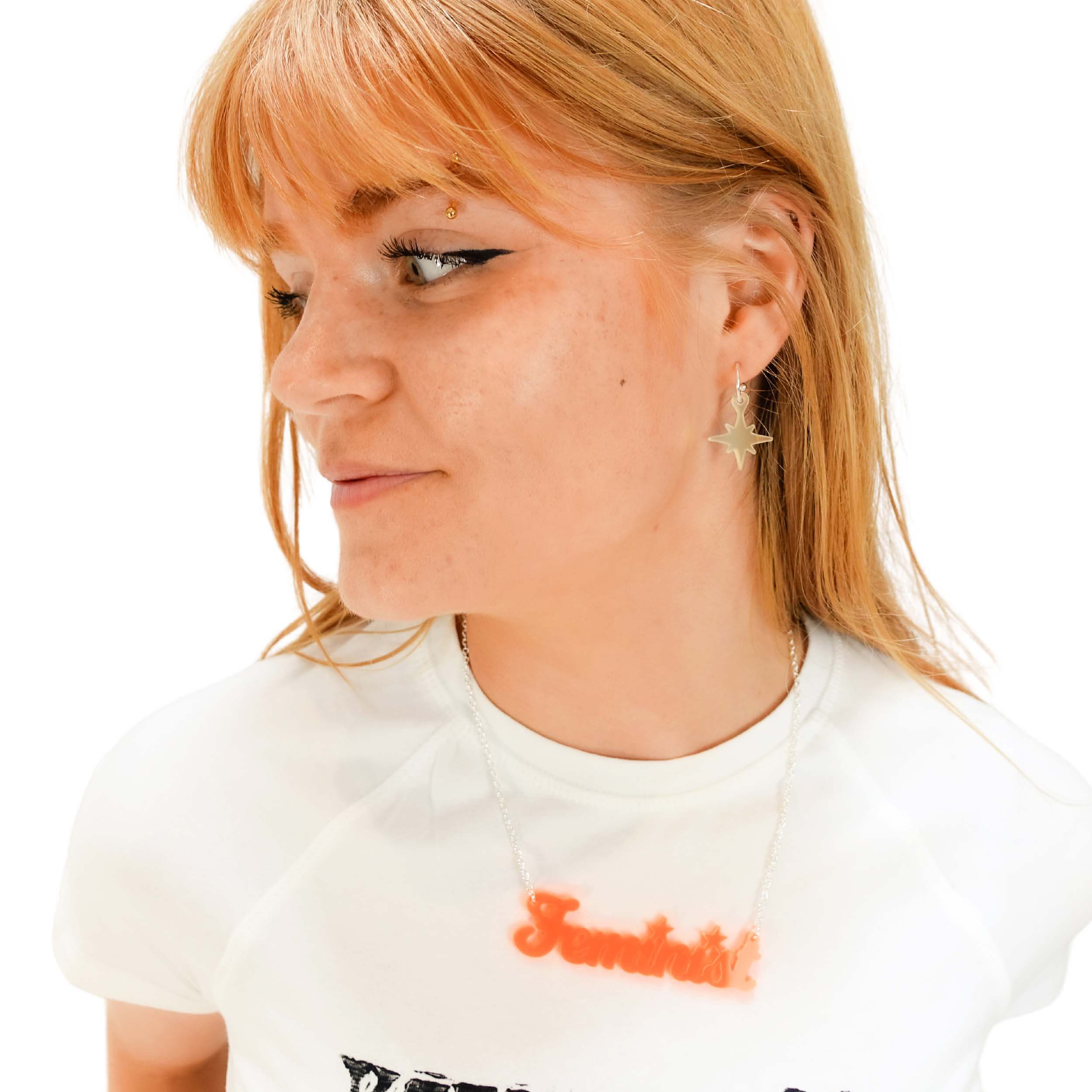 Eliza wears vintage star earrings in matte iridescent with a fluoro  orange Feminist necklace.