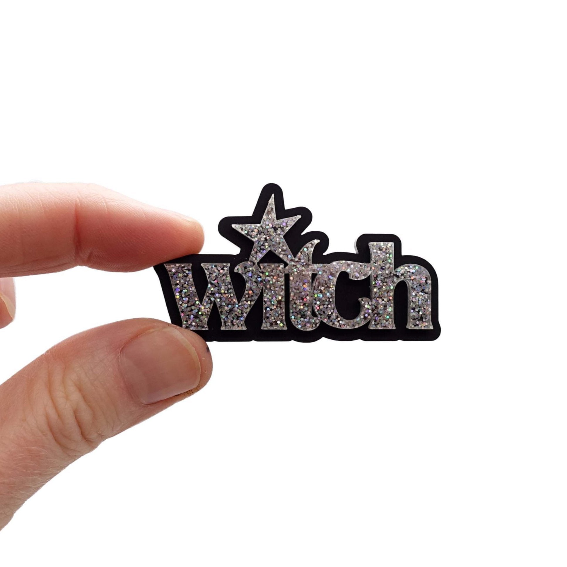 Witch brooch in silver glitter, shown held up in Sarah's fingers for scale. £2 goes to Welsh Women's Aid.