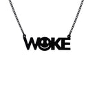 A matte black WOKE necklace with a 90s smiley face cut out of the O shown hanging on a black chain against a white background.