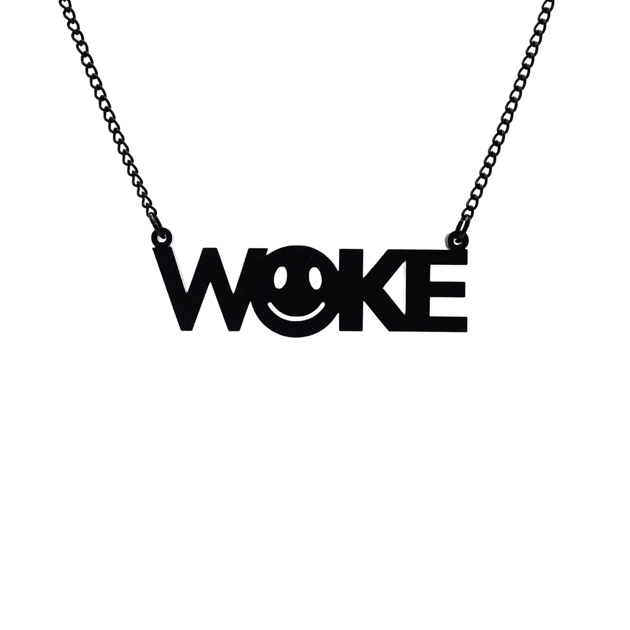 A matte black WOKE necklace with a 90s smiley face cut out of the O shown hanging on a black chain against a white background.