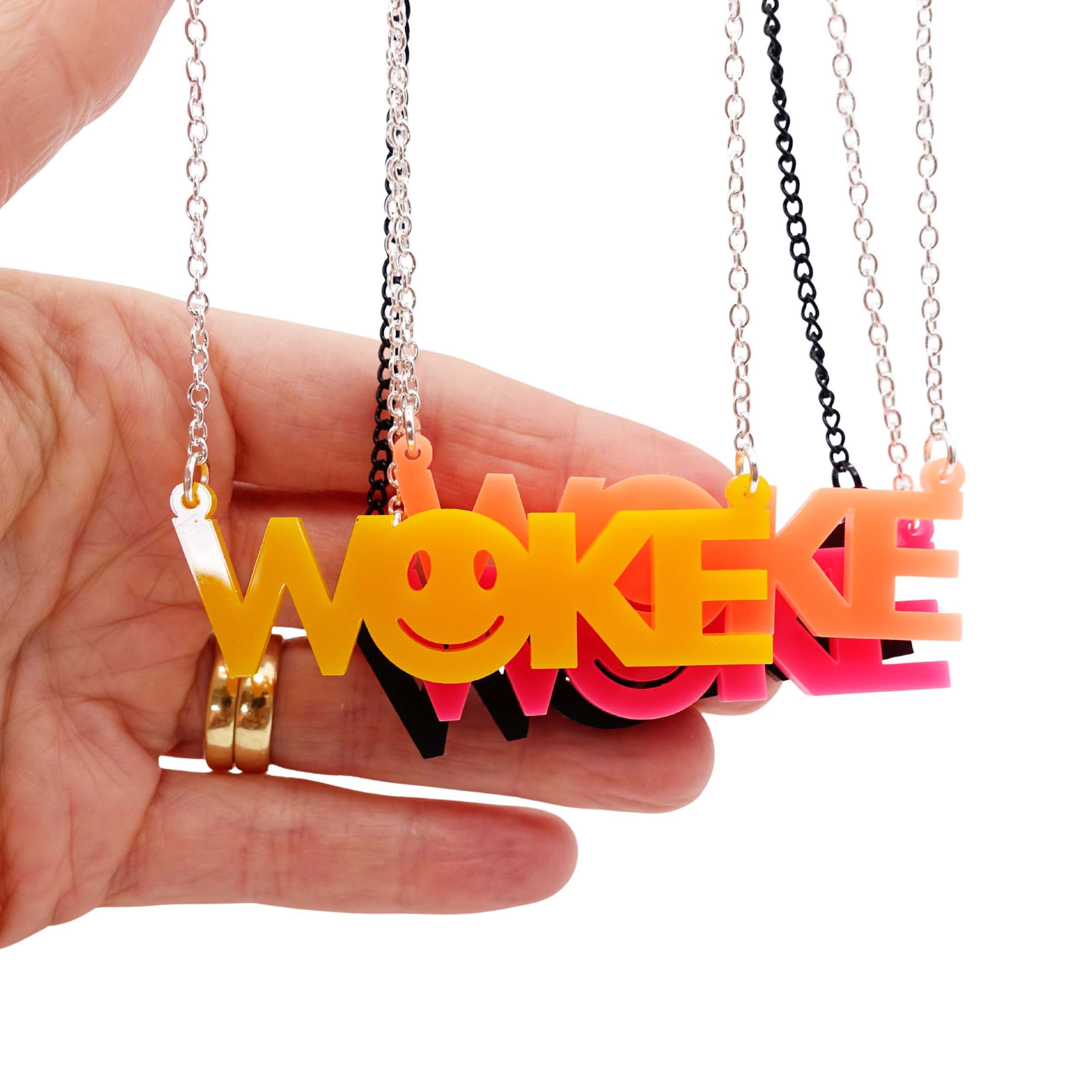A group of WOKE necklaces shown hanging with my hand for scale with yellow in front.
