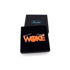A flouro orange WOKE necklace with a 90s smiley face cut out of the O shown in a Wear and Resist gift box.