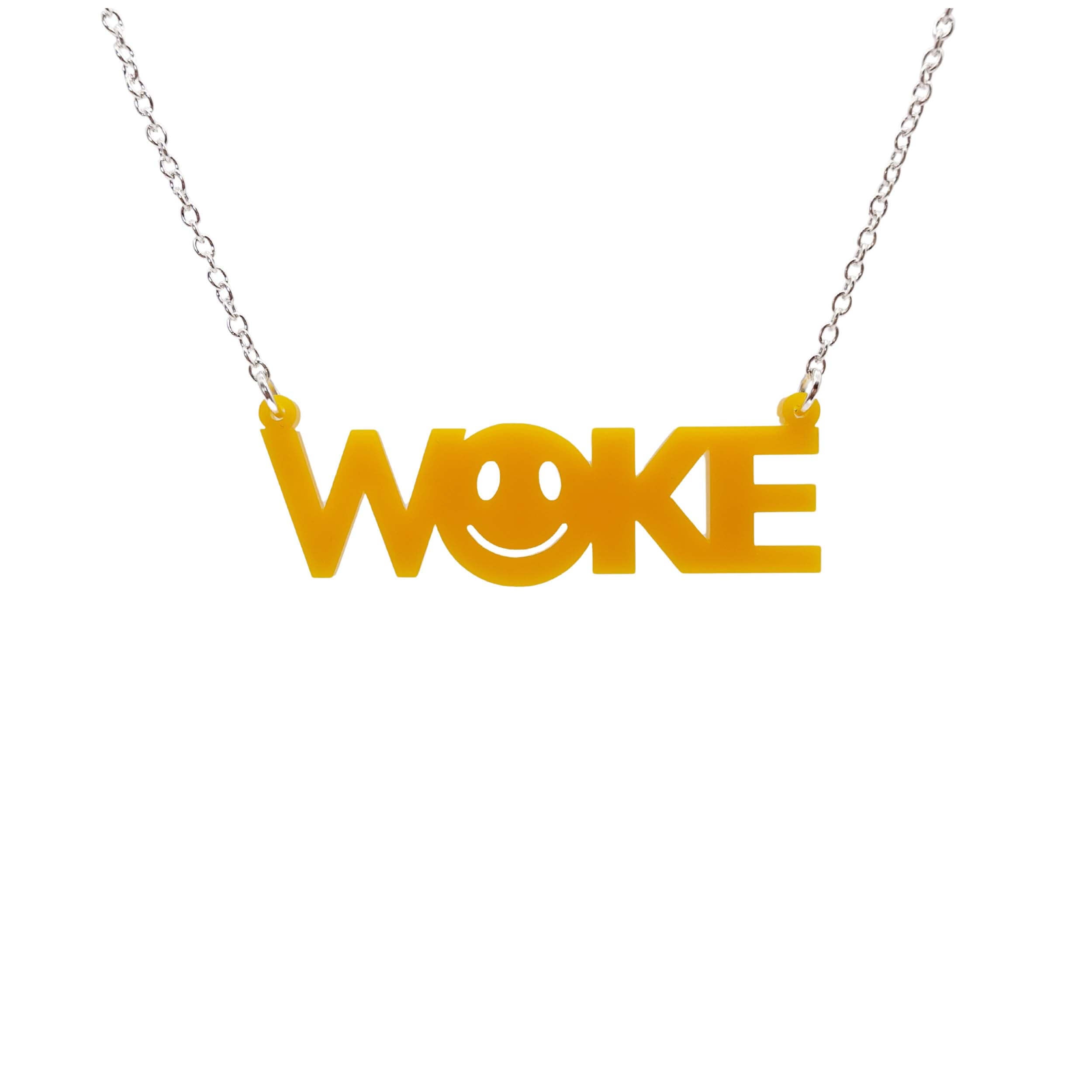 A yellow necklace of the word WOKE with a 90s smiley face cut out of the O, shown hanging on a white background.