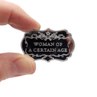 A small mirror brooch etched with the words Woman of a  Certain Age.