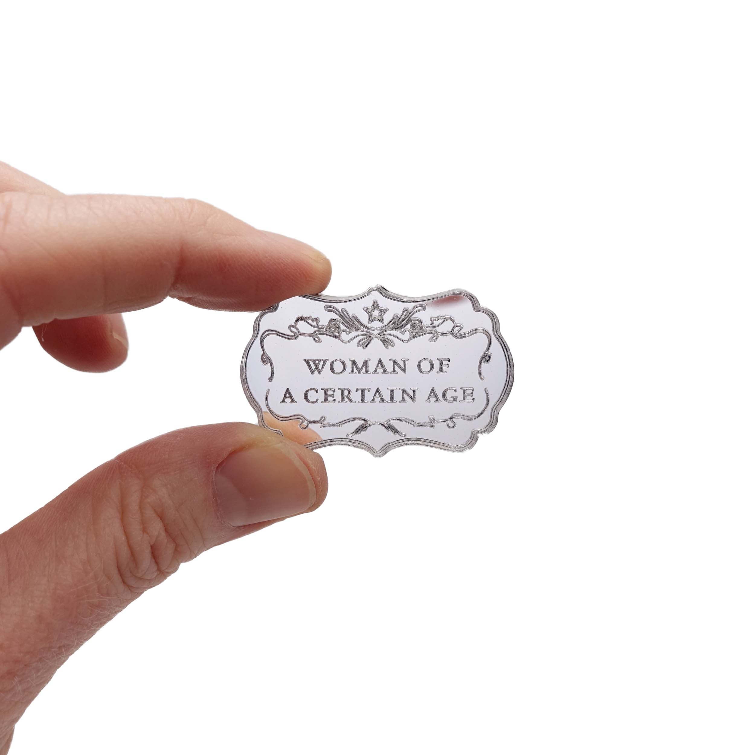 Hand holding a small silver mirror Woman of a Certain Age brooch etched with flourishes and a small star.