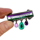 My hand holding up the Women Count brooch to the light to show the detail. The top of it was based on Sylvia Pankhurst's Hunger Strike medal.