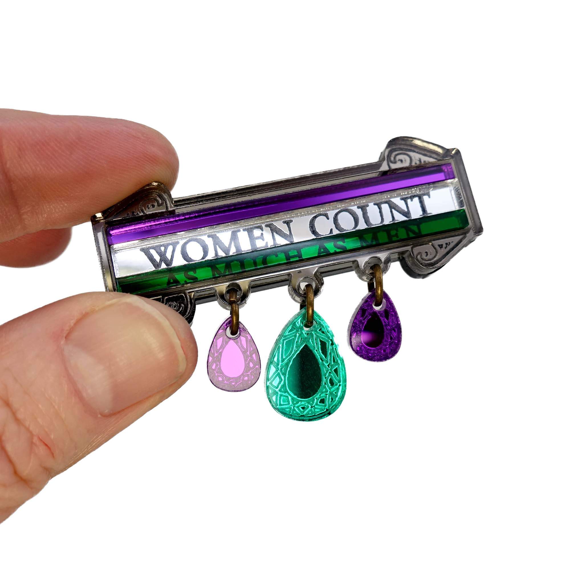 My hand holding up the Women Count brooch to the light to show the detail. The top of it was based on Sylvia Pankhurst's Hunger Strike medal.