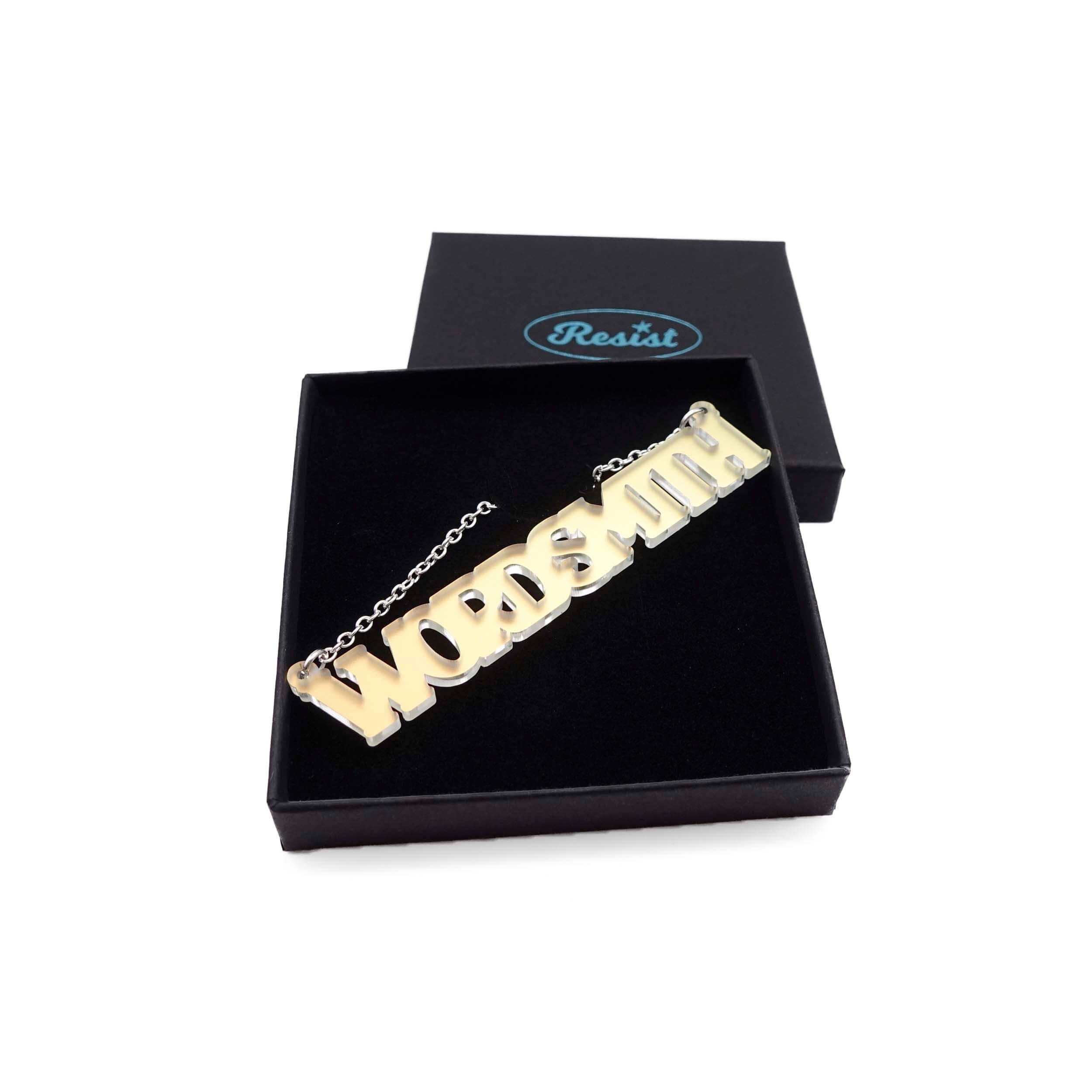 A necklace that says 'Wordsmith' in matte iridescent, shown in a Wear and Resist gift box.