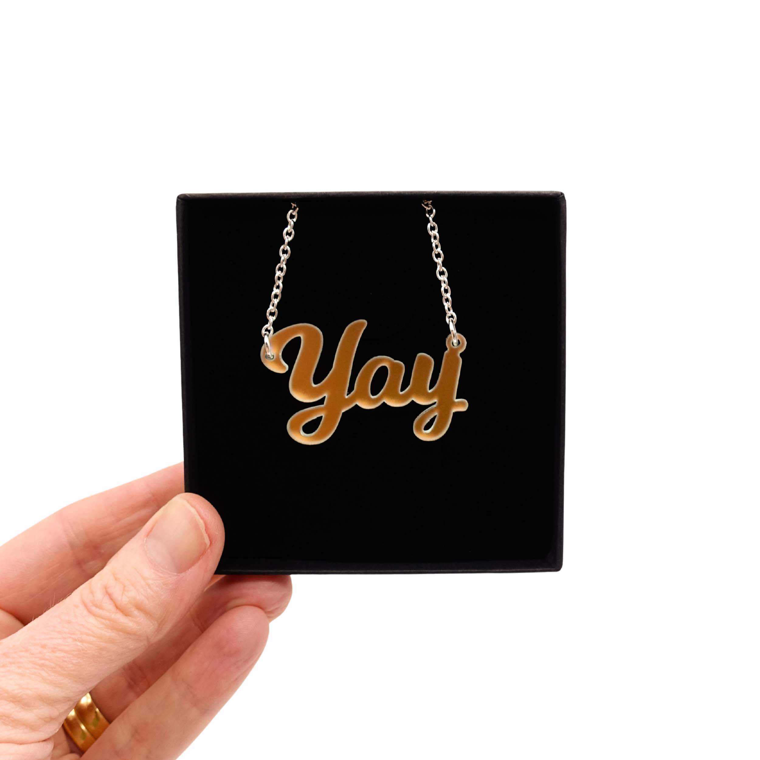 Yay necklace in matte iridescent shown held up in a Wear and Resist gift box.