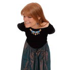 Eliza bends forward in a beautiful satin skirt ready for the ball wearing her Belle Epoque necklace in soft blue and matching large Belle Époque earrings in cool sky.