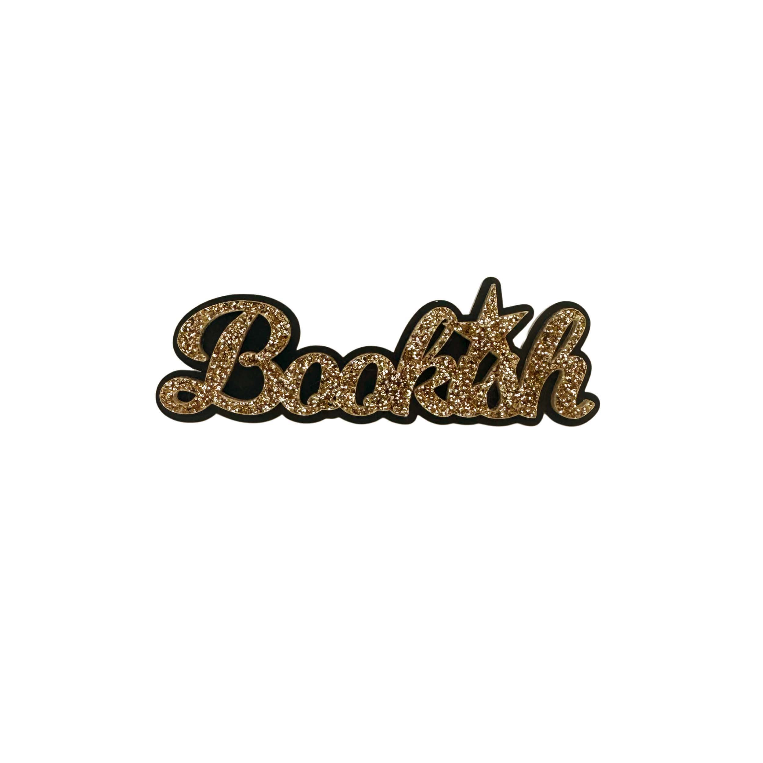Bookish brooch in gold glitter shown on a white background.