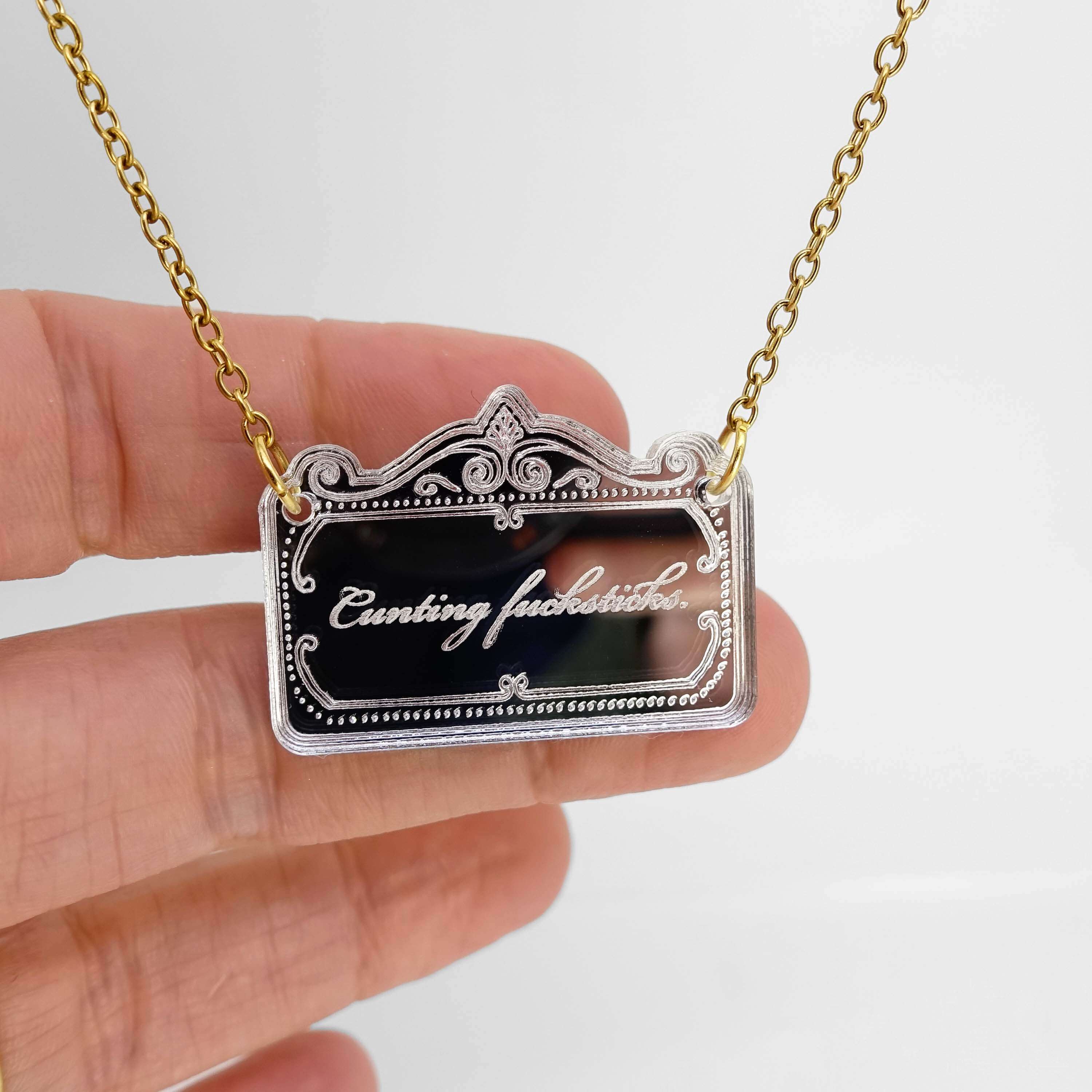 A very sweary florid necklace shown etched in silver mirror hanging on a gold plated chain with my hand behind for scale.