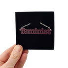 Cassis Feminist necklace shown held up in a Wear and Resist gift box.