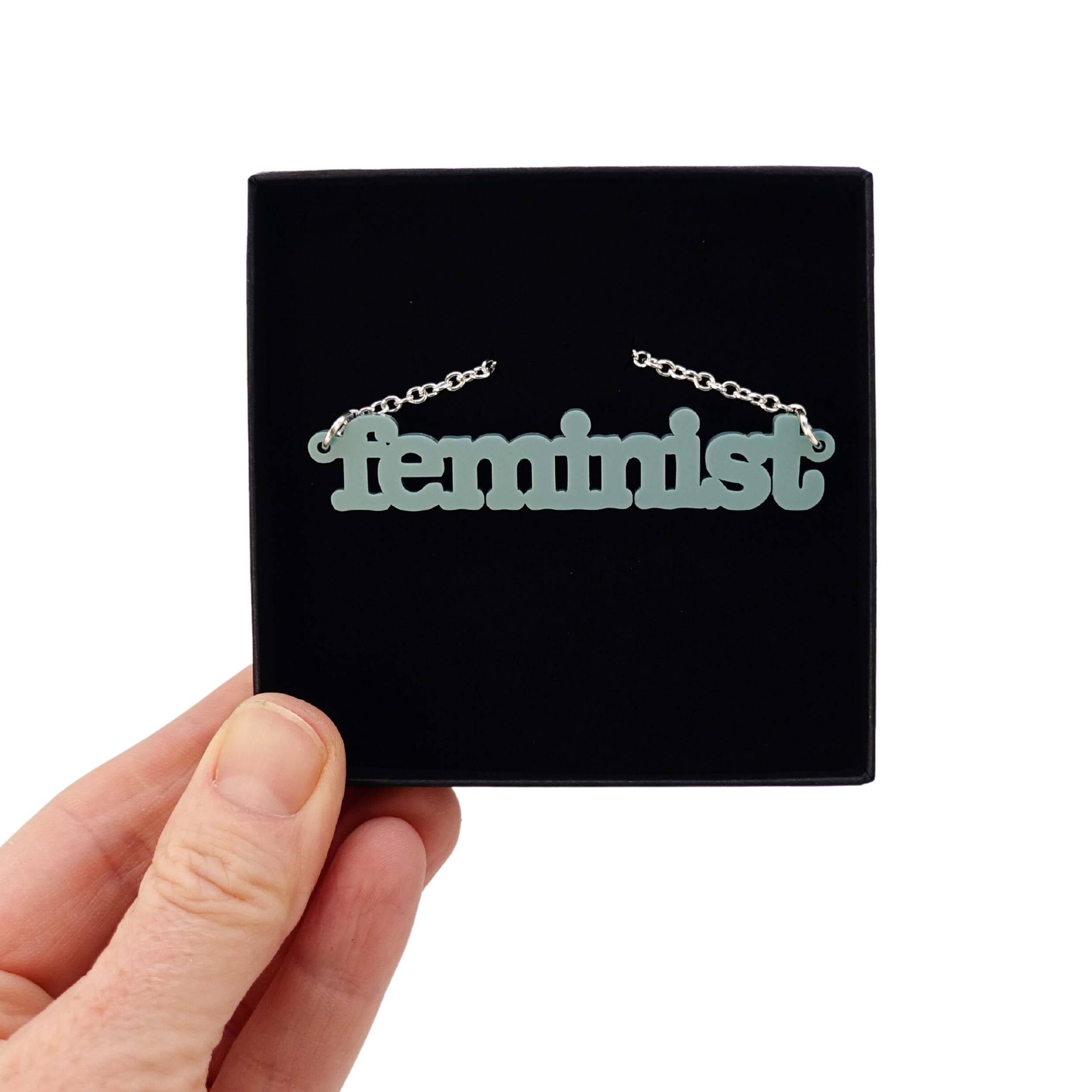 Duck egg green Feminist necklace shown held up in a Wear and Resist gift box.