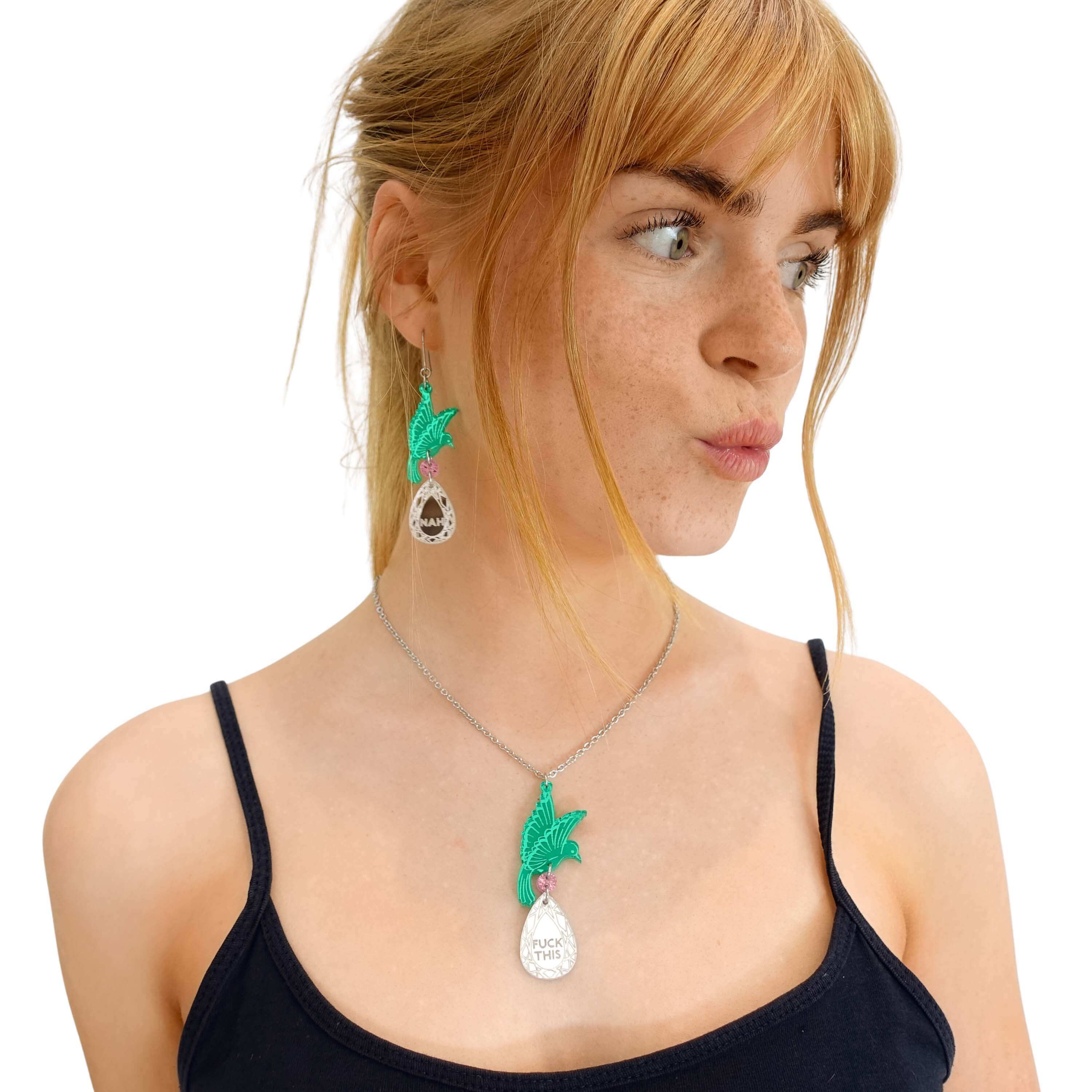 Eliza wears a green Rude Bird pendant necklace that says 'F*ck this' with matching green earrings.