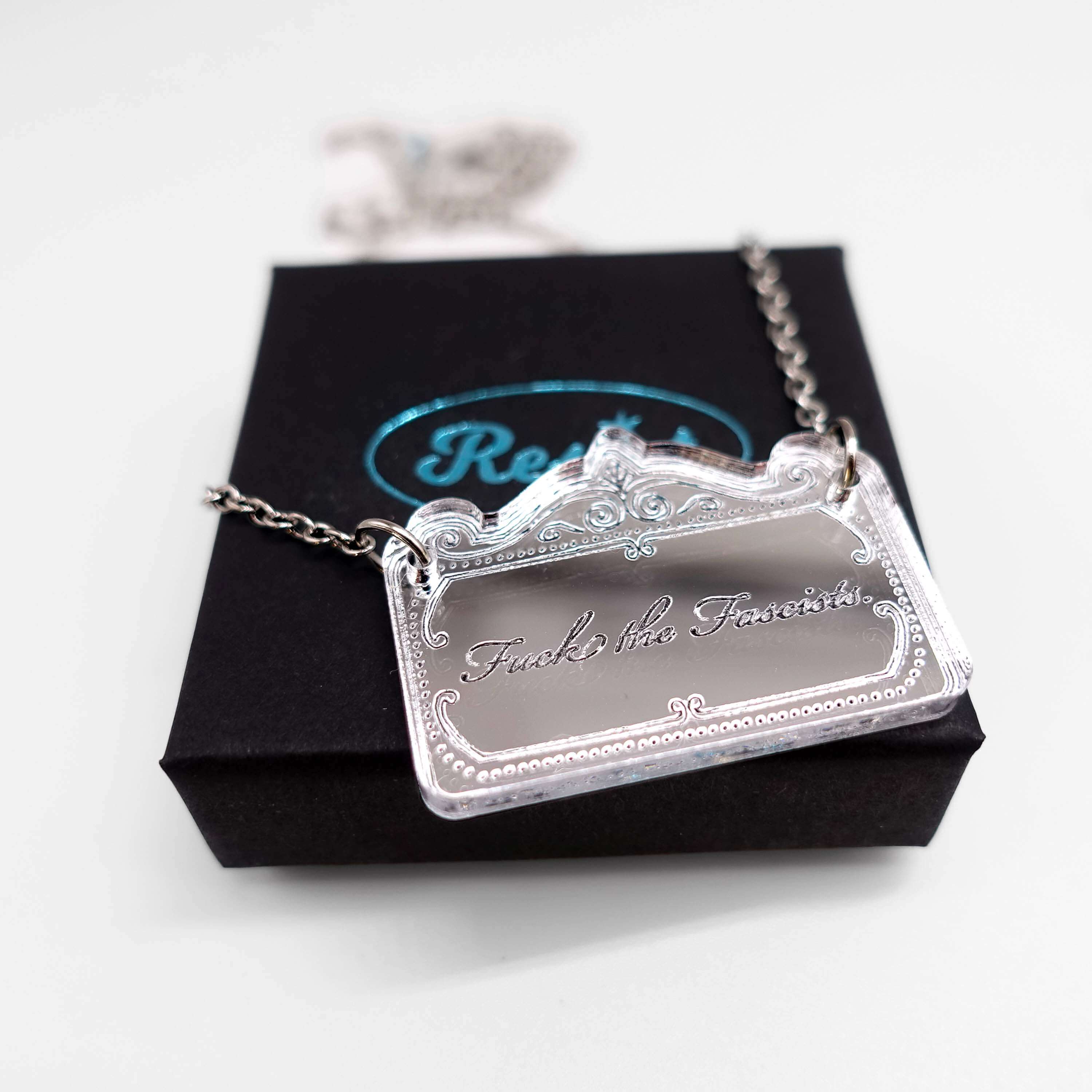 A sweary necklace etched with 'fuck the fascists' shown on a small Wear & Resist gift box.