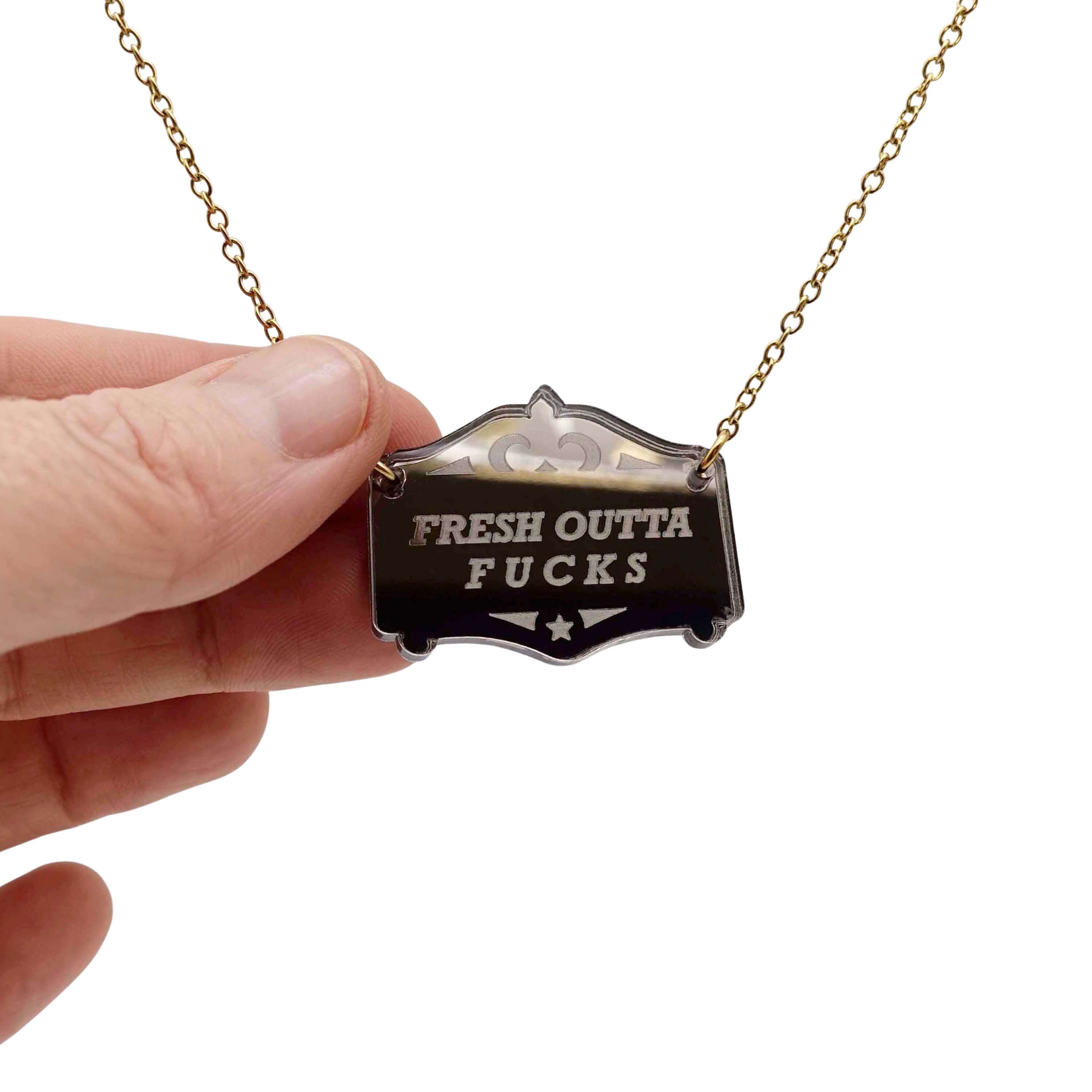 Fresh outta f*cks mirror cowboy necklace in bronze, shown hanging on a gold-plated stainless steel chain with my hand for scale.