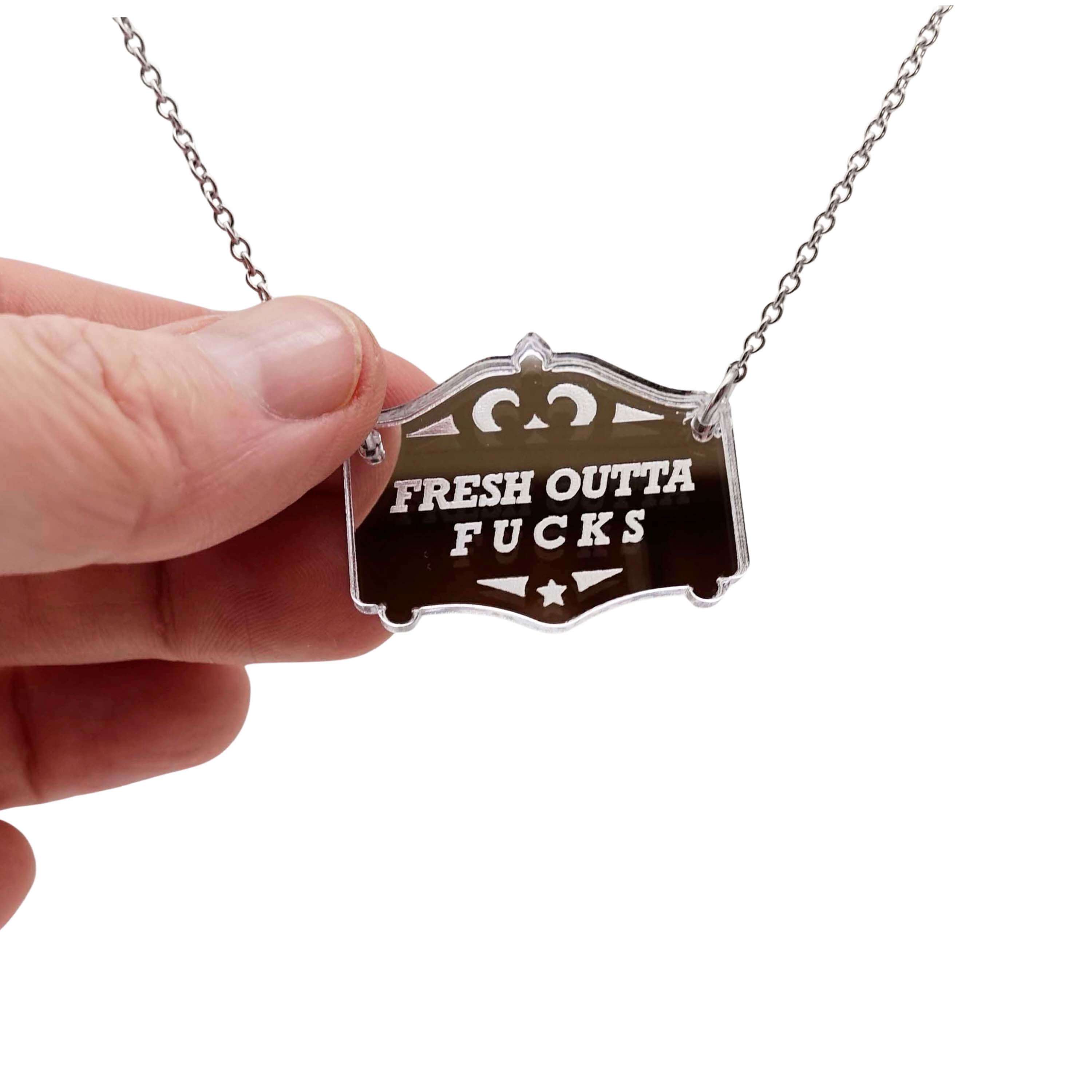 Fresh outta f*cks mirror cowboy necklace in silver, shown hanging on a stainless steel chain with my hand for scale.