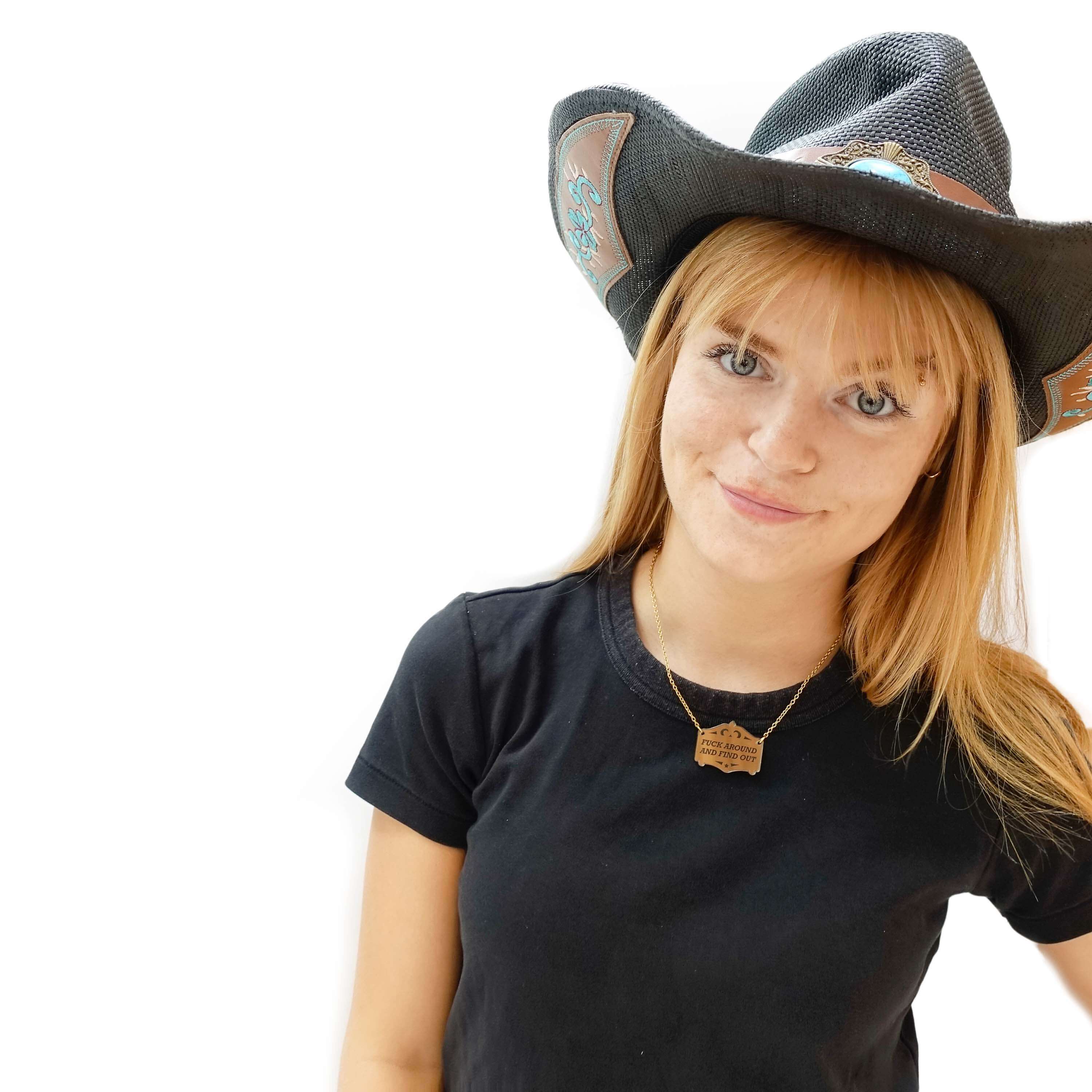 Eliza wears a F*ck around and find out mirror cowboy necklace in bronze on a gold plated chain.