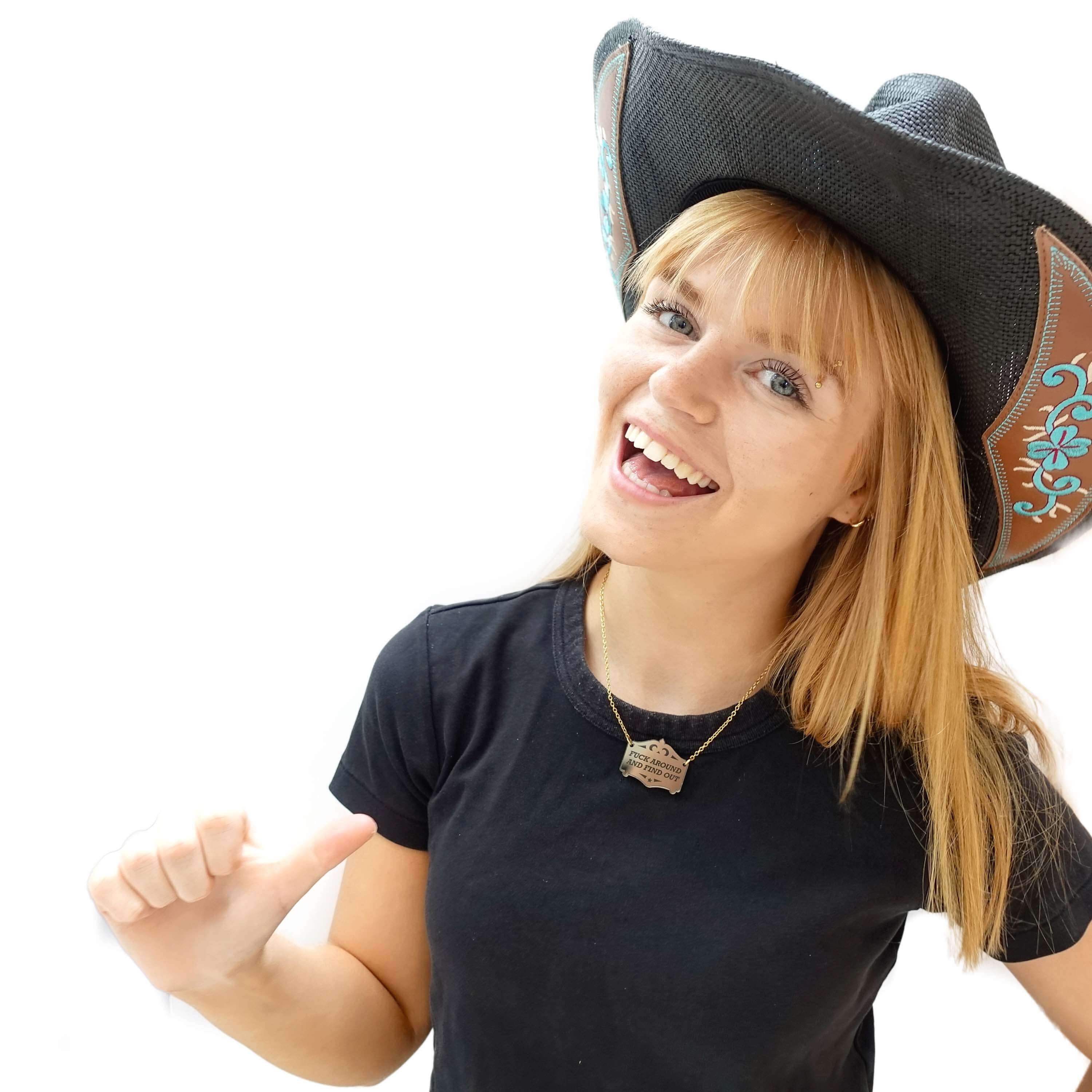 Eliza laughs, wearing a F*ck around and find out mirror cowboy necklace in bronze on a gold-plated stainless steel chain.